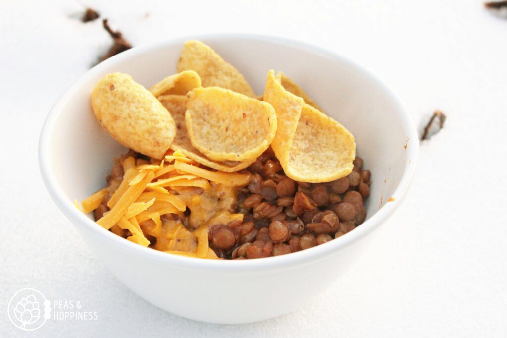 Bowl of Lentil Frito Pie topped with Fritos and Cheese sitting in the snow