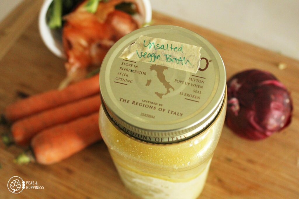 Mason jar with label on the lid that reads: Unsalted Veggie Broth with vegetables scraps laying on a cutting board in the background